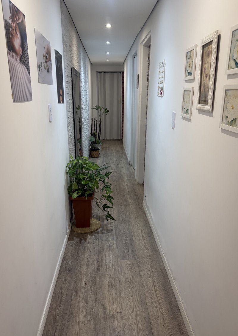 O corredor de chegada do consultório, com plantas no chão e quadros de flores nas paredes claras.