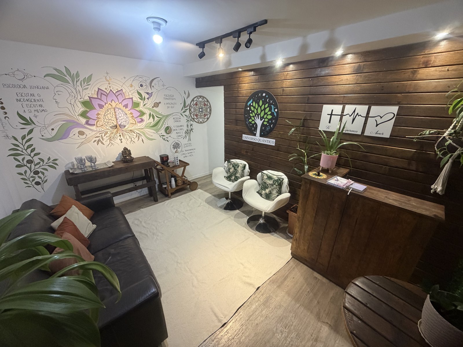 Recepção do Universoo Quântico: parede de madeira com o logo, poltronas brancas e uma parede viva de folhagem com flores.