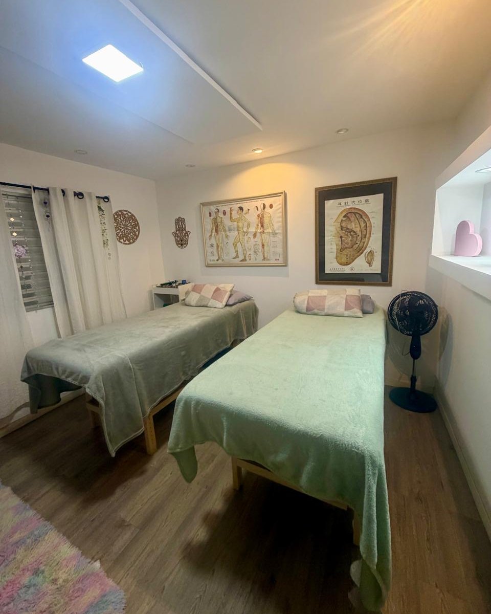 A sala das práticas integrativas: duas macas com mantas verdes e os mapas de pontos de acupuntura emoldurados na parede.